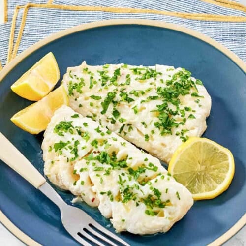 Lemony butter white fish and lemon wedges on a plate.