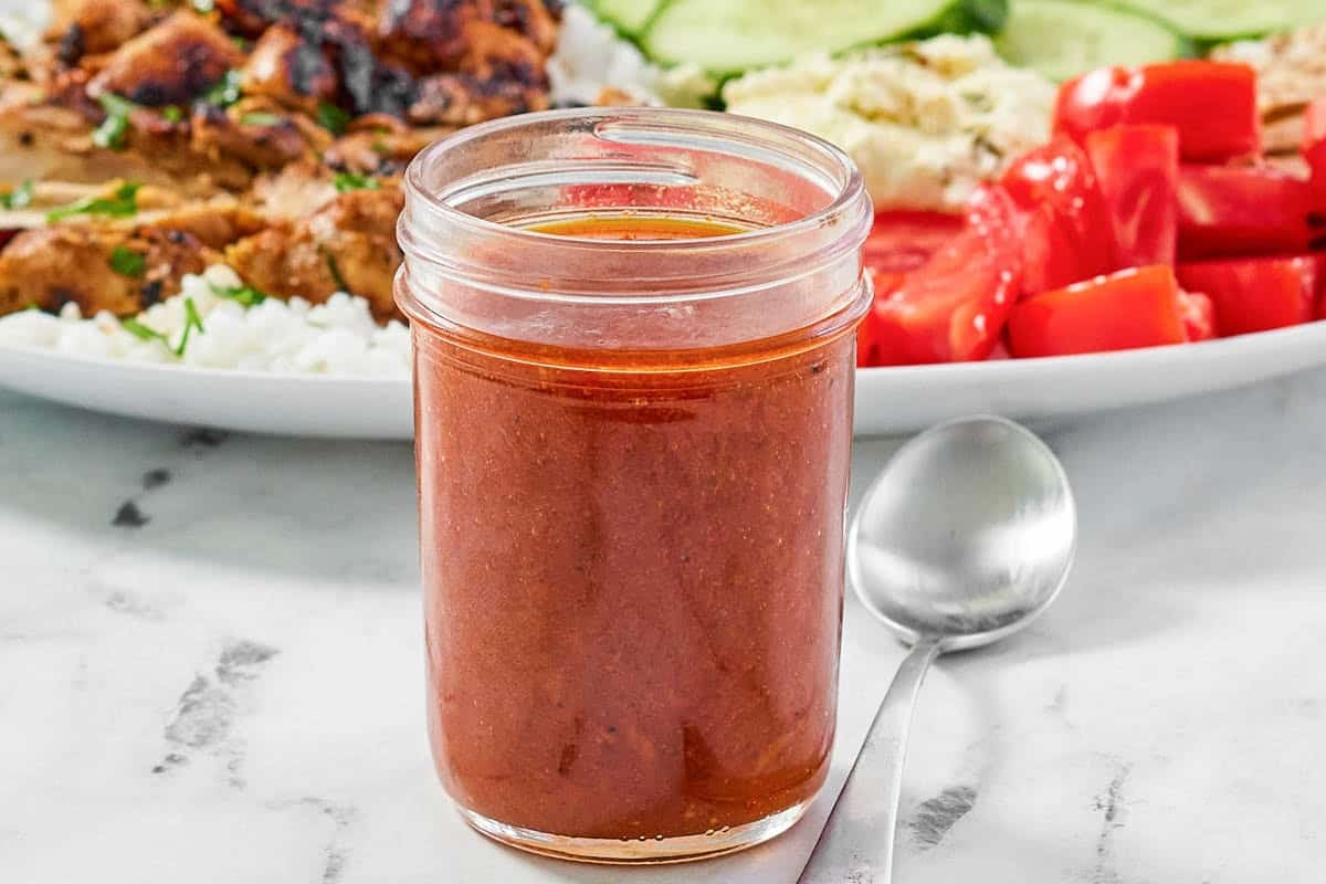 Mediterranean spicy dressing in a mason jar in front of a salad.