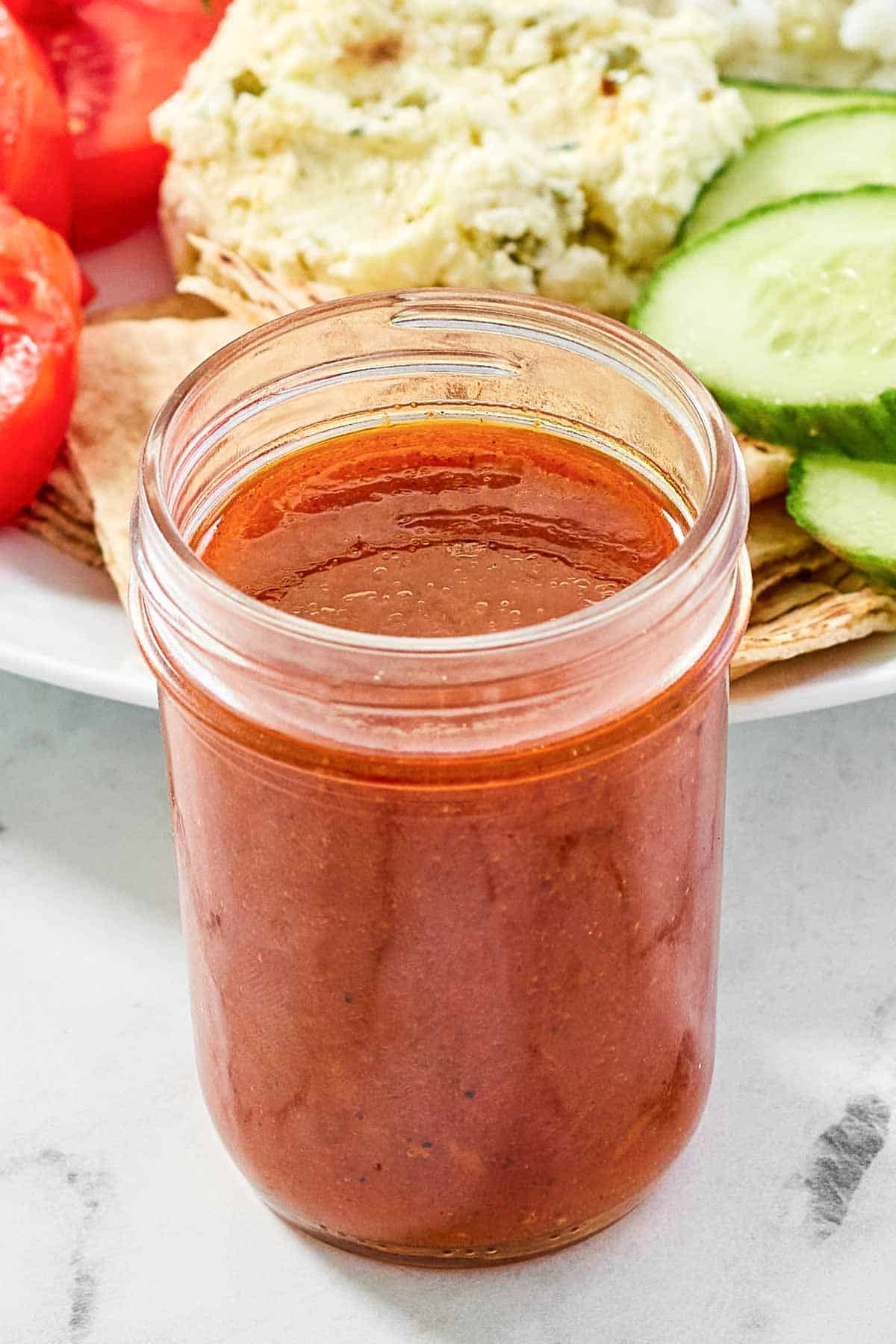 A jar of tangy and spicy vinaigrette in front of a Mediterranean salad.