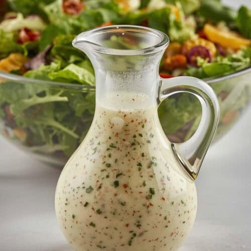 Vinaigrette dressing in a small pitcher and a salad behind it.