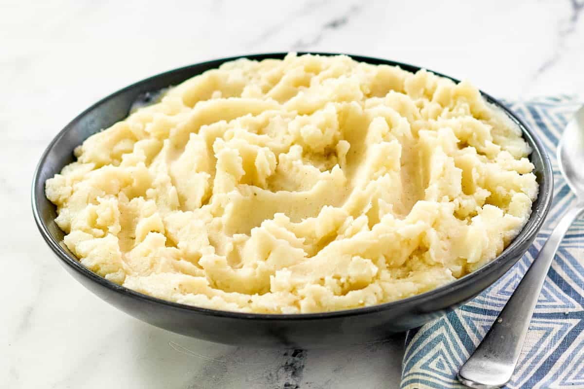 A bowl of buttery mashed potatoes on a marble surface.