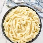 A bowl of buttery whipped potatoes with a spoon resting on a napkin beside it.
