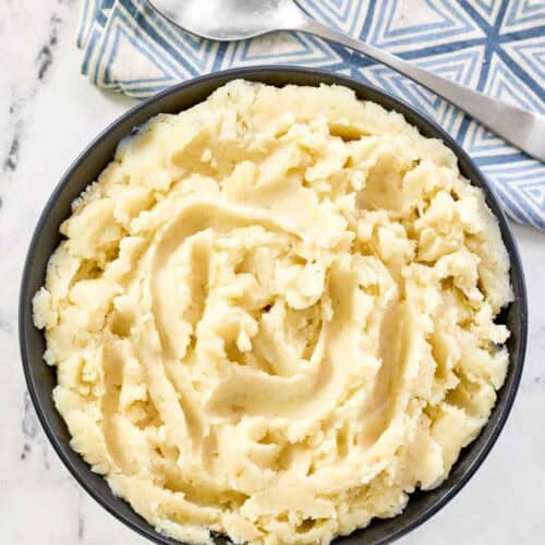 A bowl of buttery whipped potatoes with a spoon resting on a napkin beside it.