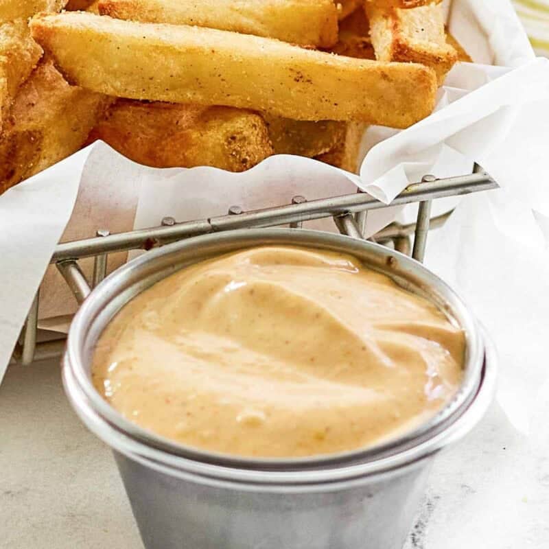 French fries in a parchment lined wire basket and a small cup of creamy seasoned dipping sauce.