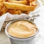 Copycat Freddy's fry sauce in a small cup and French fries in a serving basket.