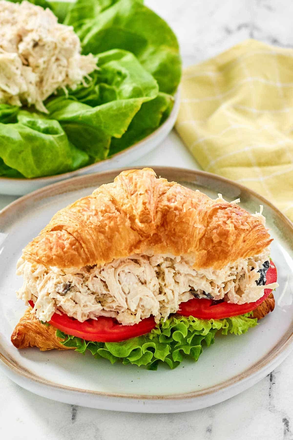 Greek chicken salad croissant sandwich with lettuce and tomato.