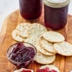Jars of homemade wine jelly and crackers on a wood serving board.