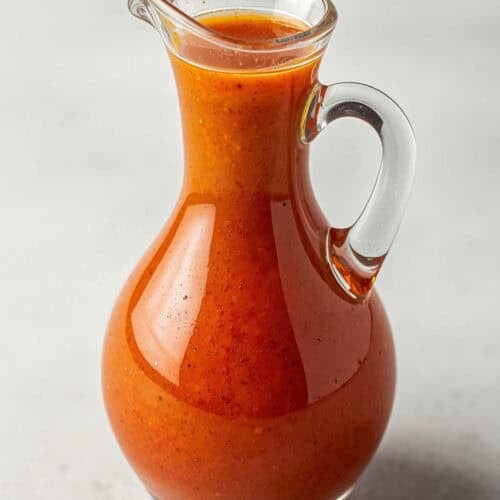 A small pitcher of tomato-based salad dressing.