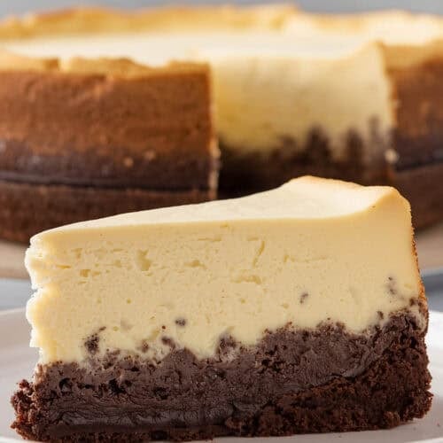 A slice of brownie bottom cheesecake on a plate and the cheesecake behind it.