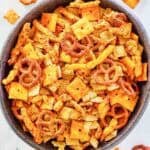 A bowl of cheddar snack mix with cereal, crackers, pretzels, and cheese puffs.