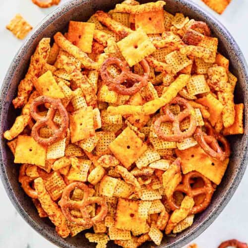 A bowl of cheddar snack mix with cereal, crackers, pretzels, and cheese puffs.