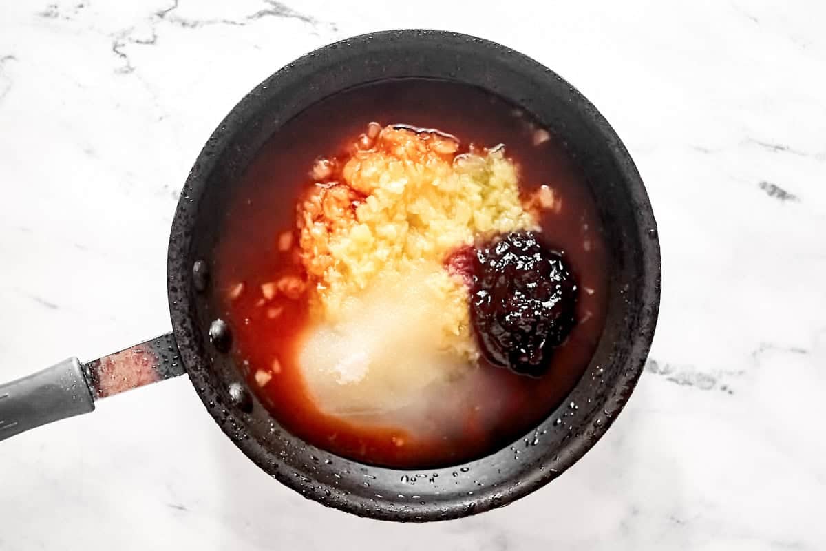 Cooking plum preserves, crushed pineapple, sugar, and sweet and sour sauce in a skillet.