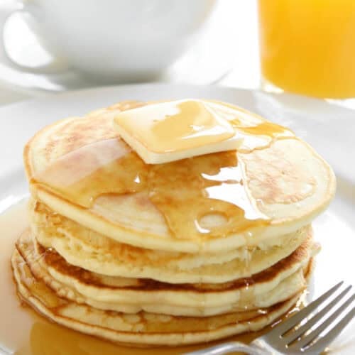 A stack of pancakes topped with butter and syrup, cup of coffee, and glass of orange juice.