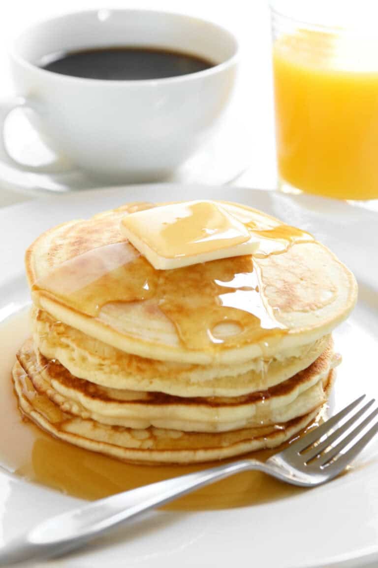 A stack of pancakes topped with butter and syrup, cup of coffee, and glass of orange juice.