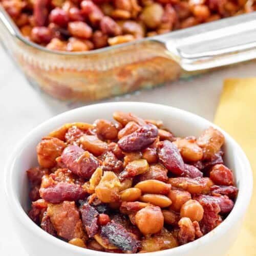Five bean casserole with bacon in a bowl and glass baking dish.