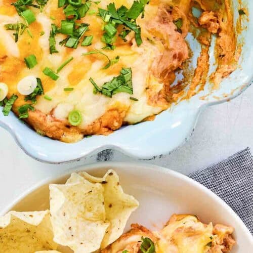 Refried bean cream cheese taco dip in a baking dish and served with tortilla chips.