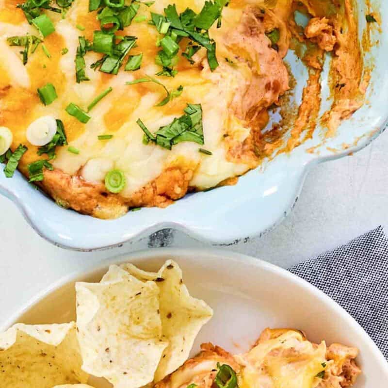 Refried bean cream cheese taco dip in a baking dish and served with tortilla chips.