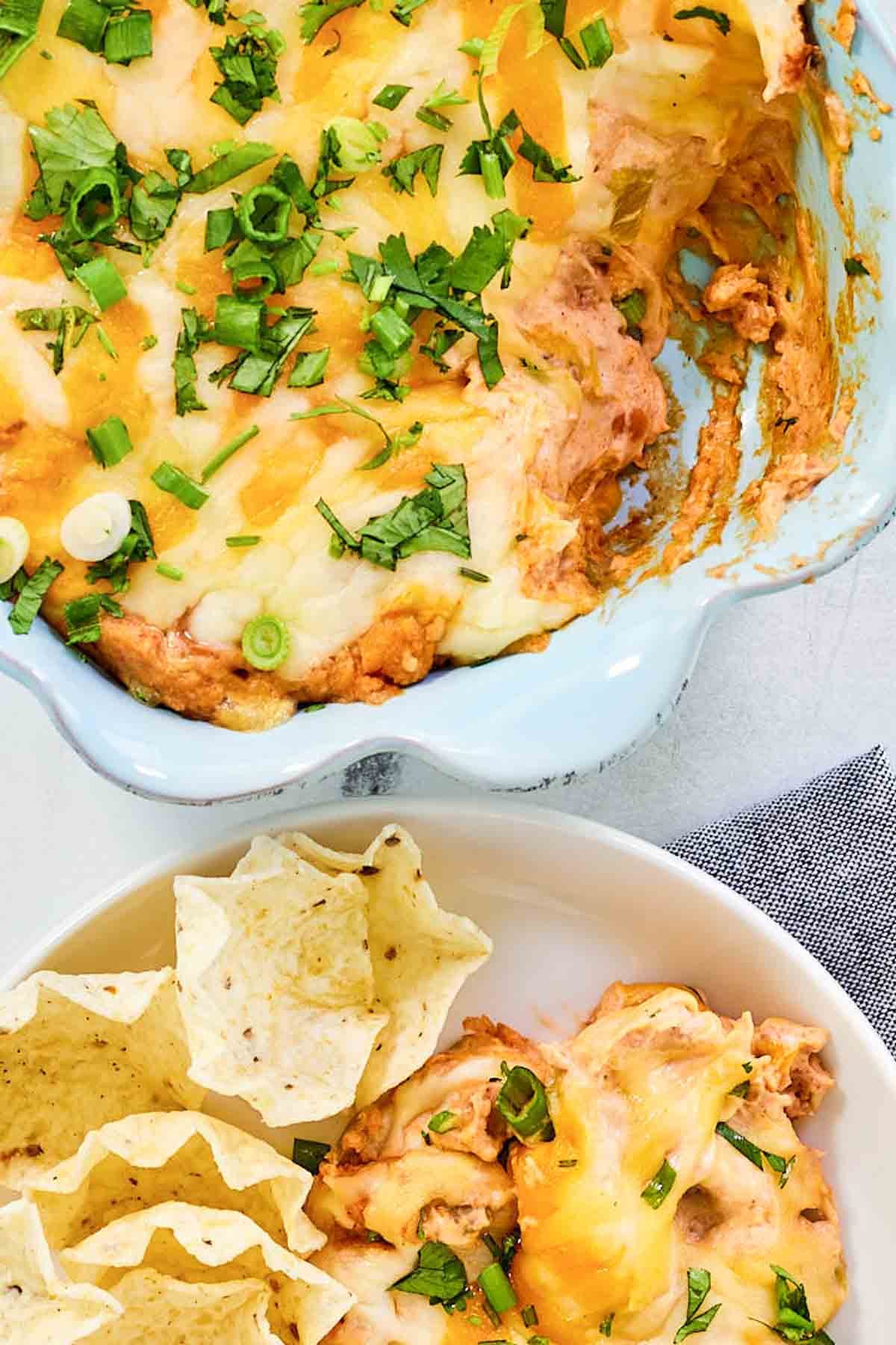 Refried bean cream cheese taco dip in a baking dish and served with tortilla chips.