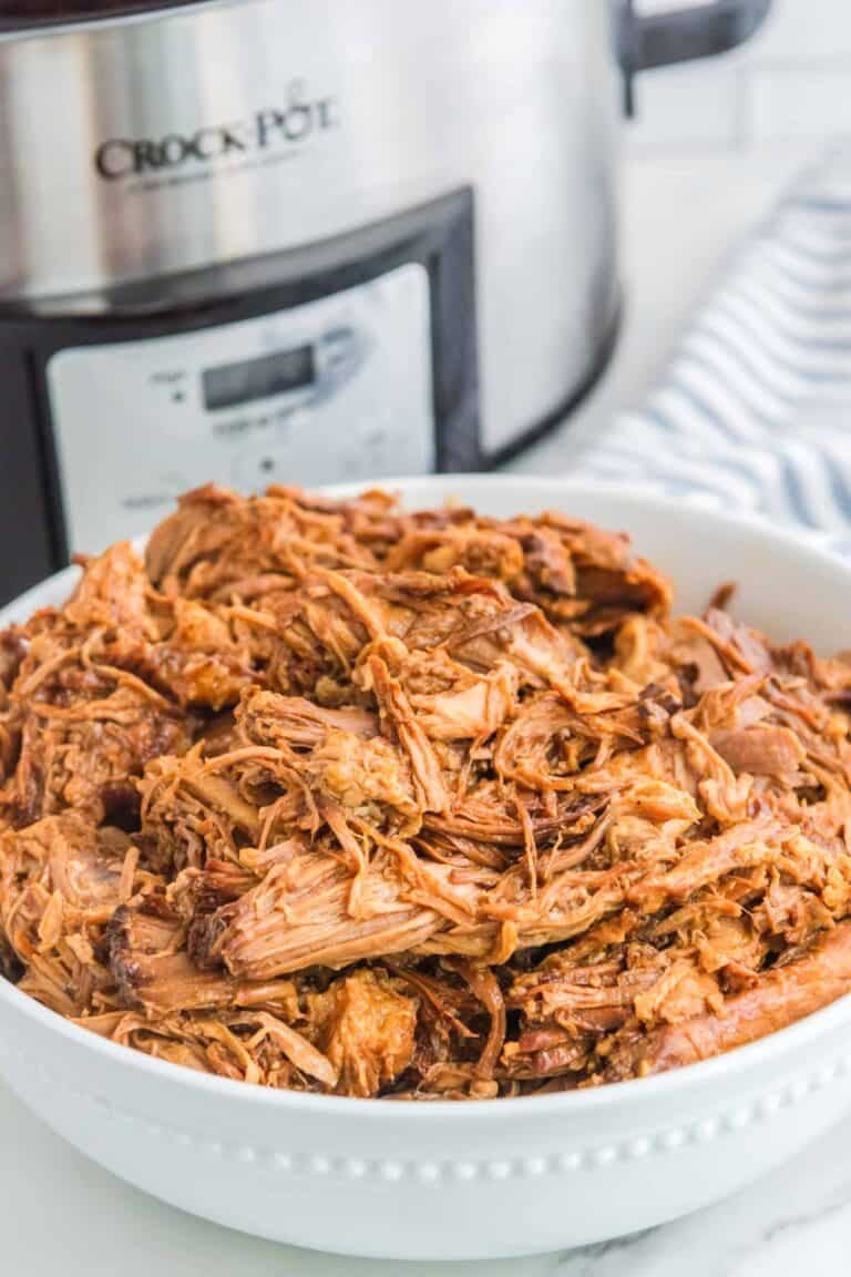 Shredded barbecue pork in a bowl and a Crock Pot behind it.