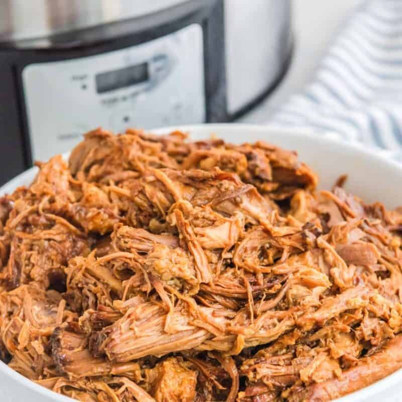Shredded barbecue pork in a bowl and a Crock Pot behind it.