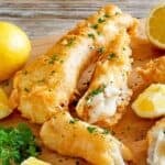 Copycat Captain D's battered fish and lemons on a wood serving board.
