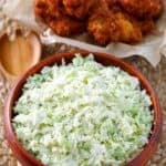 Homemade coleslaw in a bowl and a basket of chicken wings behind it.