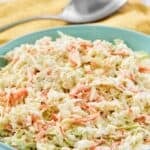 A bowl of copycat Popeyes coleslaw and a spoon on a napkin behind it.