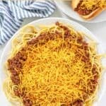 A plate of spaghetti topped with copycat Skyline chili and shredded cheese.