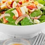 A small bowl of hot bacon dressing in front of a spinach salad.