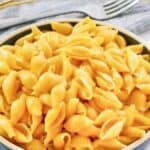 A bowl of copycat Velveeta shells and cheese and a fork on a napkin behind it.
