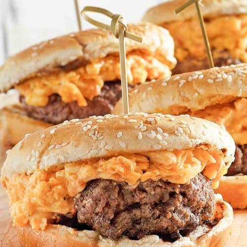 Burgers topped with pimento cheese on a wood serving board.