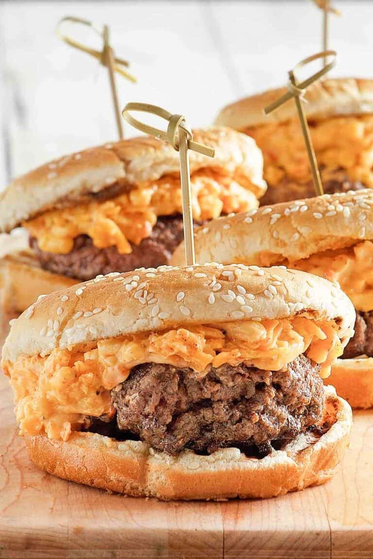 Burgers topped with pimento cheese on a wood serving board.