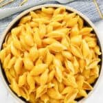 Cheesy shell pasta in a bowl and a fork on a napkin beside it.