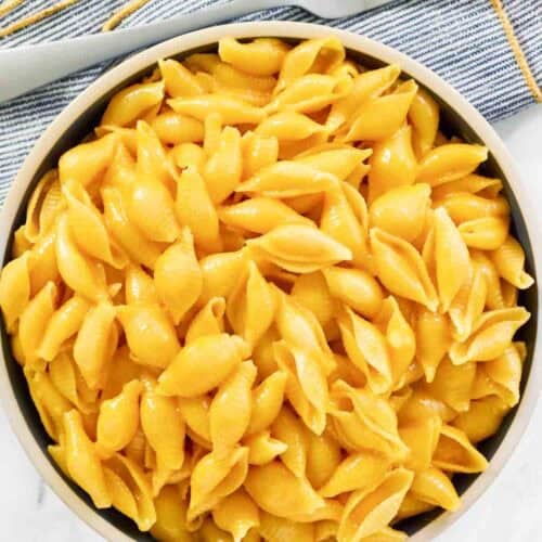 Cheesy shell pasta in a bowl and a fork on a napkin beside it.