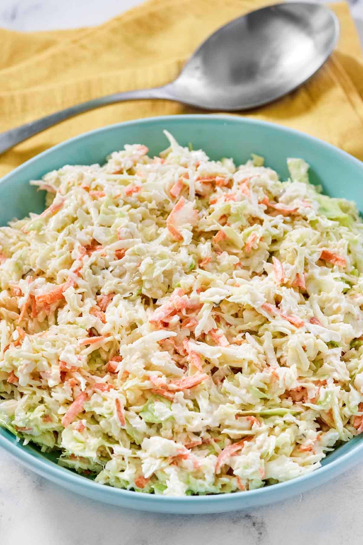 Creamy cabbage, carrot, onion, and pickle relish slaw in a bowl and a spoon resting on a napkin behind it.