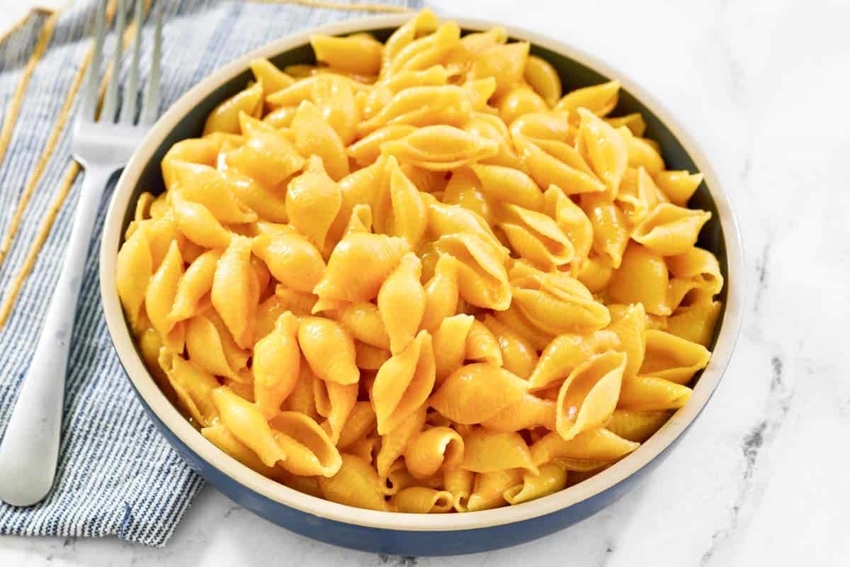 Creamy and cheesy shell pasta in a bowl and a fork resting on a napkin beside it.