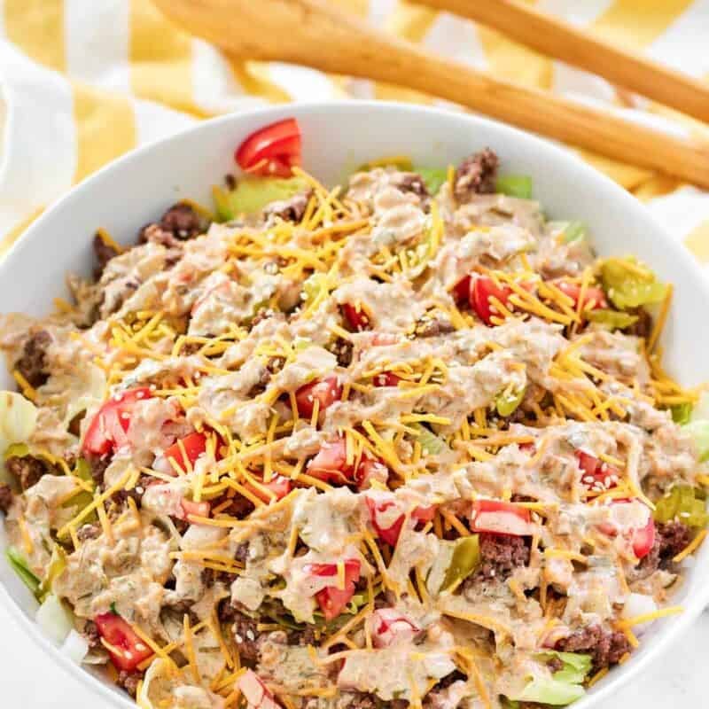 A salad with ground beef, cheese, onion, tomato, and creamy dressing.