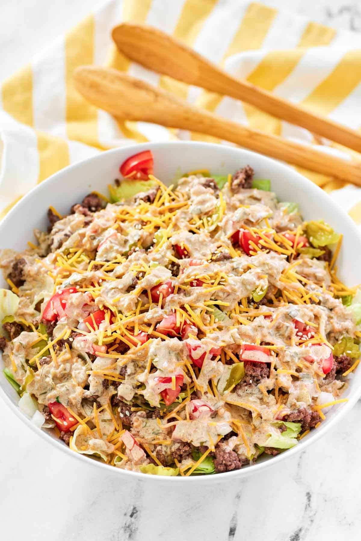 A salad with ground beef, cheese, onion, tomato, and creamy dressing.