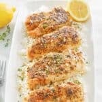 Baked lemon pepper chicken breasts served over rice on a platter.