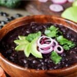 Cooked black turtle beans garnished with sliced avocado, red onion, and fresh cilantro.
