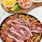 Copycat Chili's steak fajitas served with tortillas, lime wedges, shredded cheese, and pico de gallo.