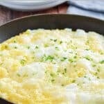 Fluffy souffle omelet in a skillet on a wooden table.