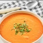 Creamy fresh tomato soup and a spoon on a napkin behind it.