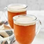 Copycat Harry Potter butterbeer is glass mugs and a kitchen towel next to them.