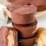 A stack of homemade Reese's peanut butter cups on a plate and one with a bite out of it leaning on the stack.