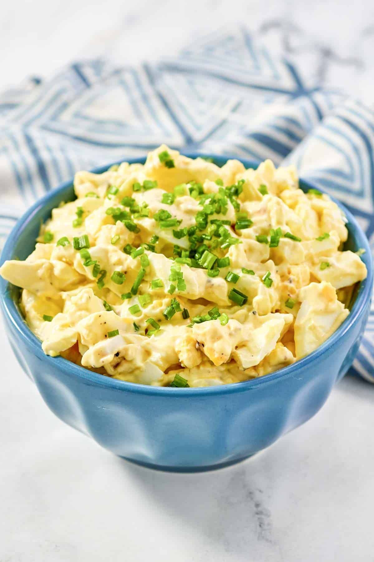 Chunky egg salad in a small bowl and a napkin beside it.