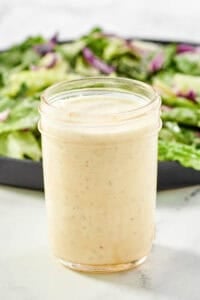 Creamy Italian dressing in a glass jar and a salad behind it.