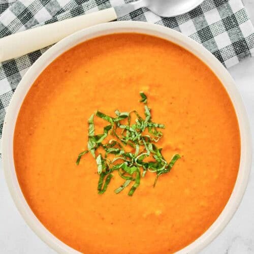 Creamy tomato soup topped with fresh basil slices.