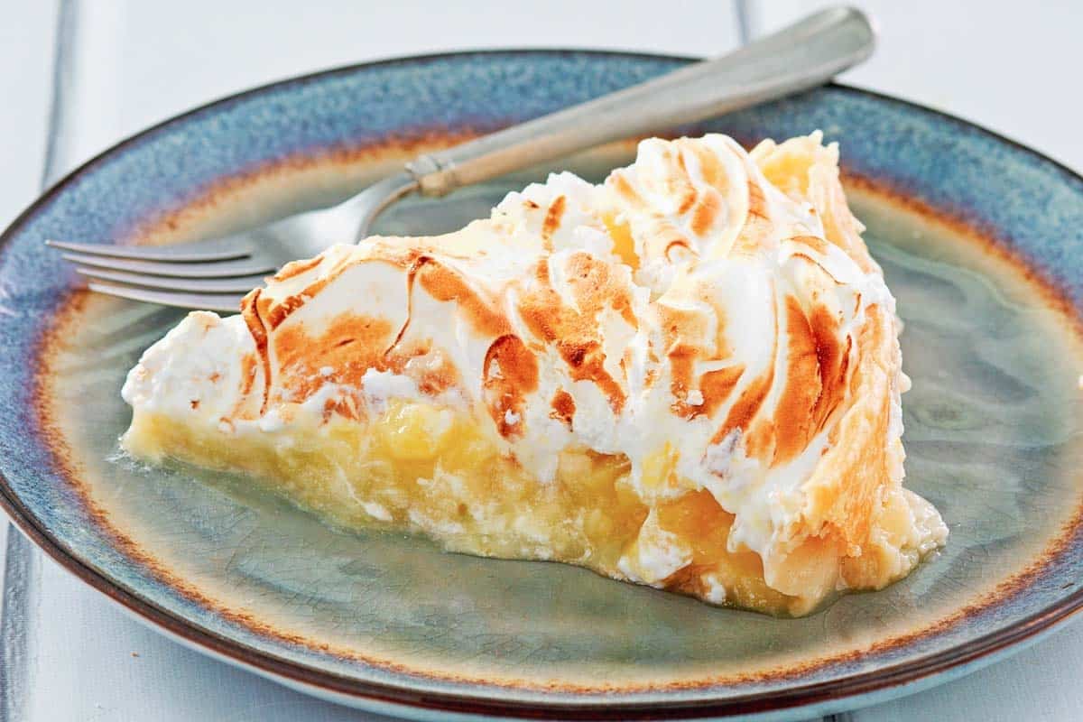 A lemon meringue pie slice and a fork on a plate.