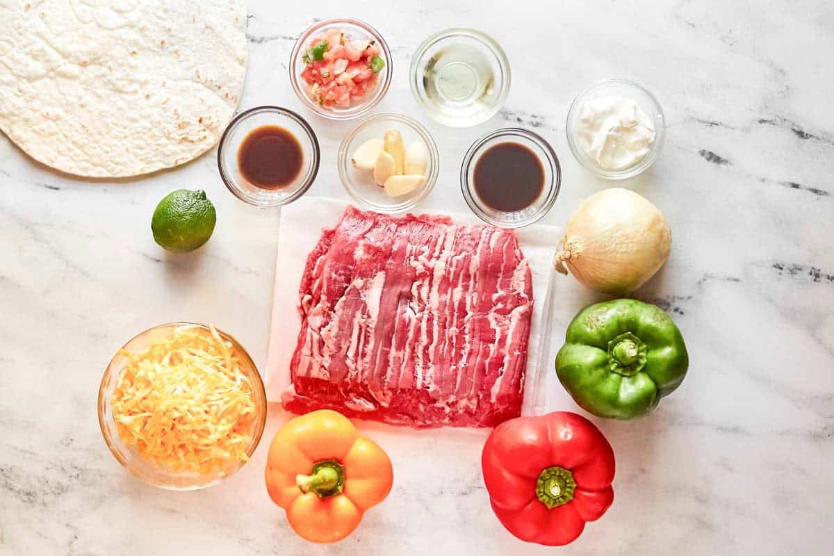 Skirt steak, onion, bell peppers, garlic, oil, lime, sauces, tortillas, cheese, and pico de gallo.
